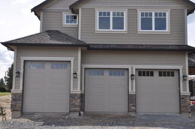 Modern three-car garage featuring beige doors with windows and stone accents