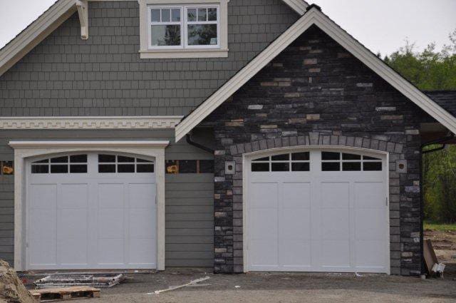 Two white garage doors are flanked by grey stone and siding on a modern home