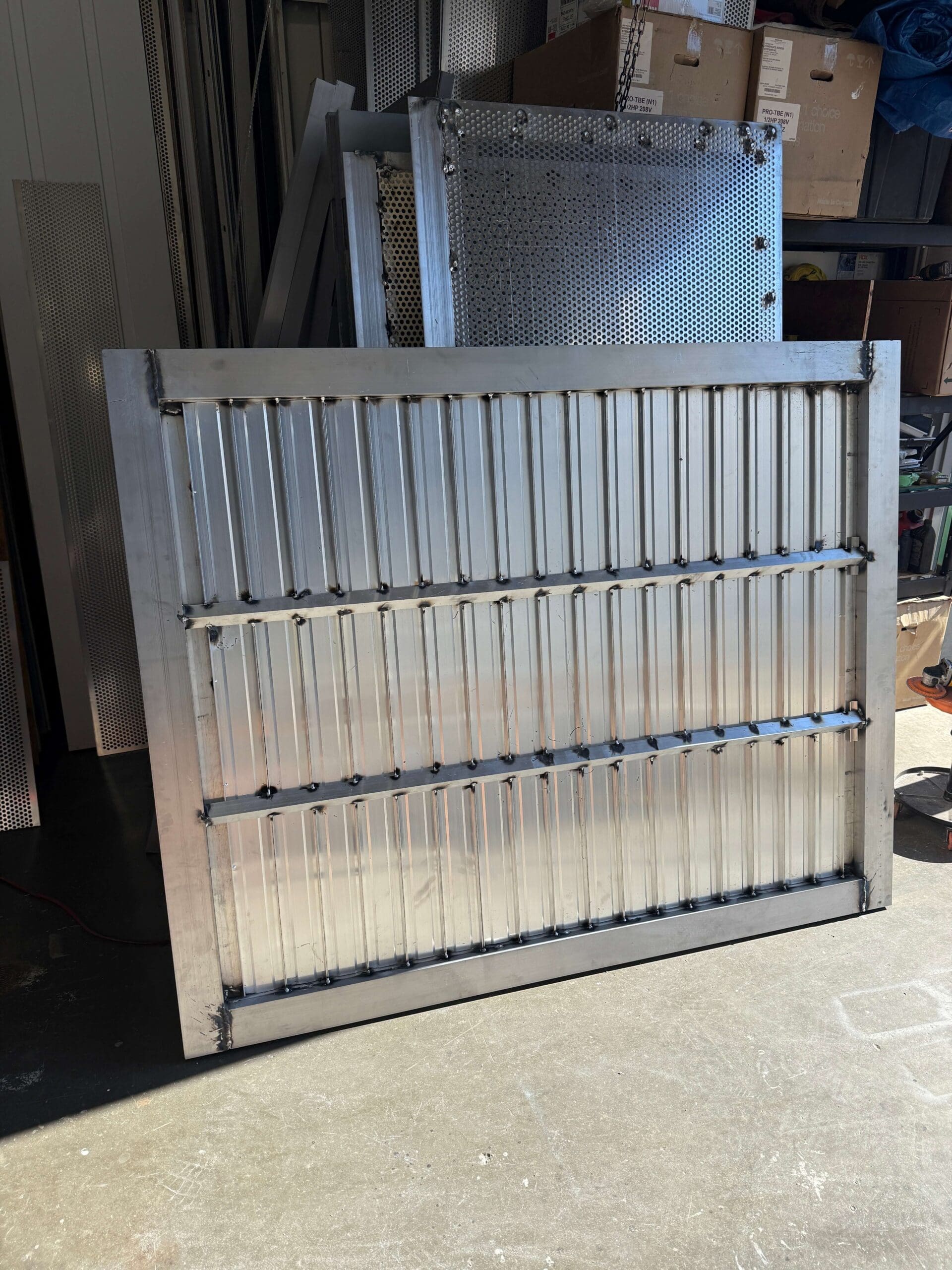 A metallic sheet with vertical ridges, featuring horizontal strips at regular intervals, leaning against a wall in a workshop setting.